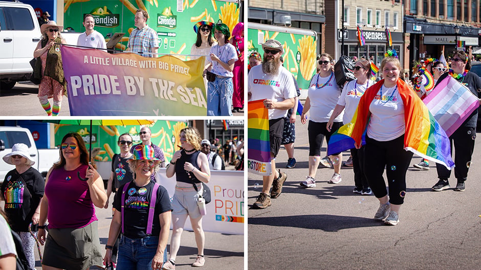 Participants march in a Pride parade carrying rainbow and trans flags, with a “Pride by the Sea” banner.